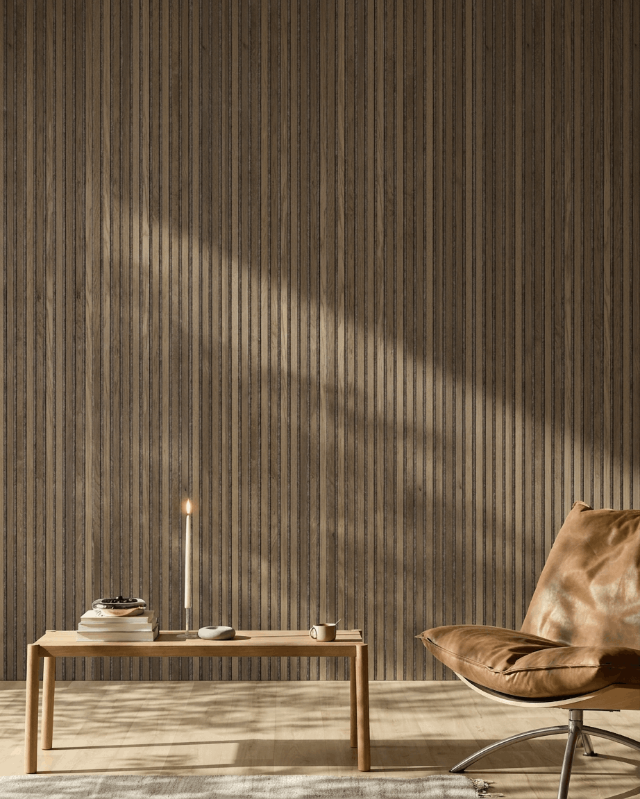 A modern room featuring a brown leather chair, wood table, and a WoodUpp Akupanel in Rustic Grey Oak mounted on the wall, illuminated by soft sunlight.